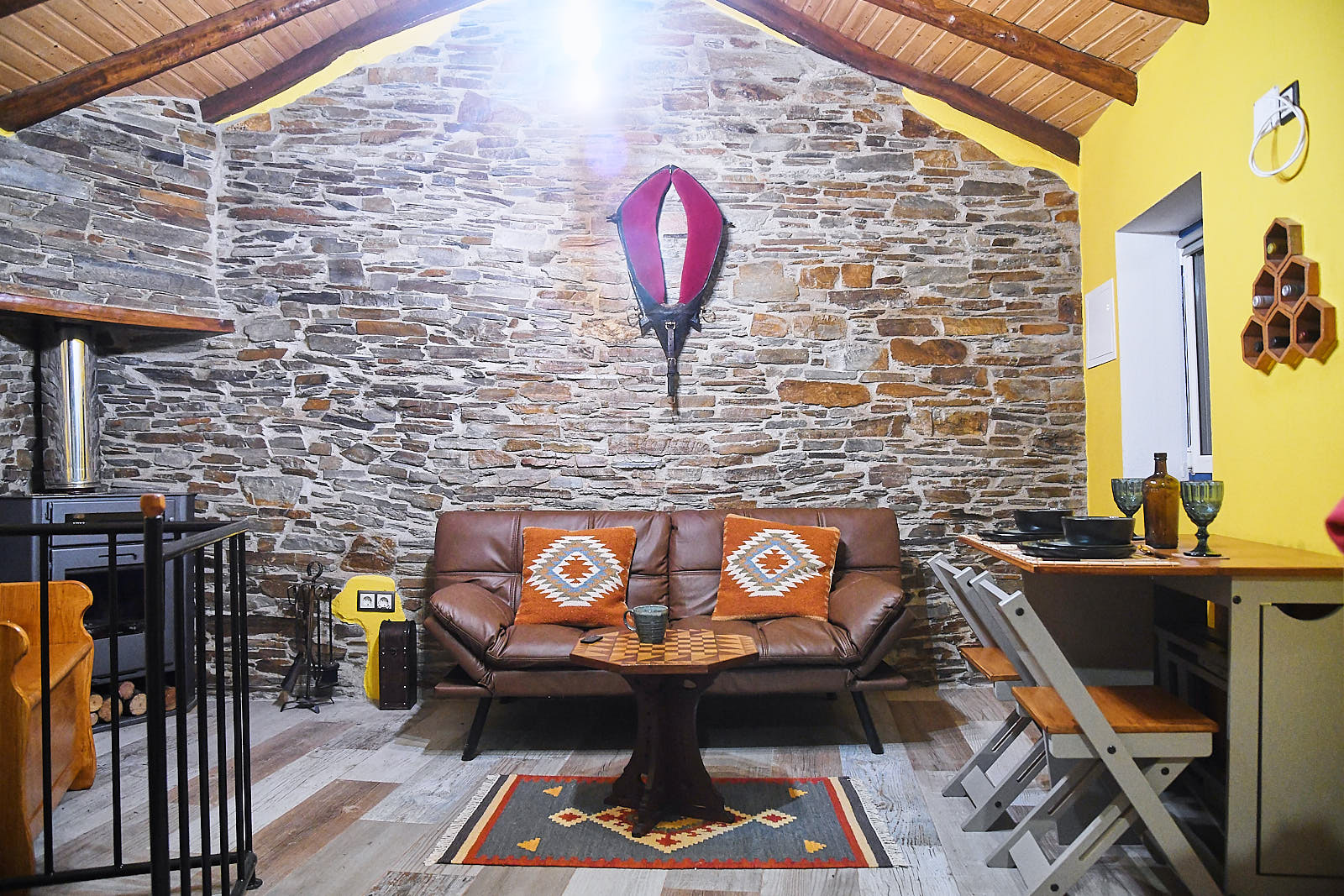 Living room with a leather sofa, patterned cushions and dining table against an exposed stone wall