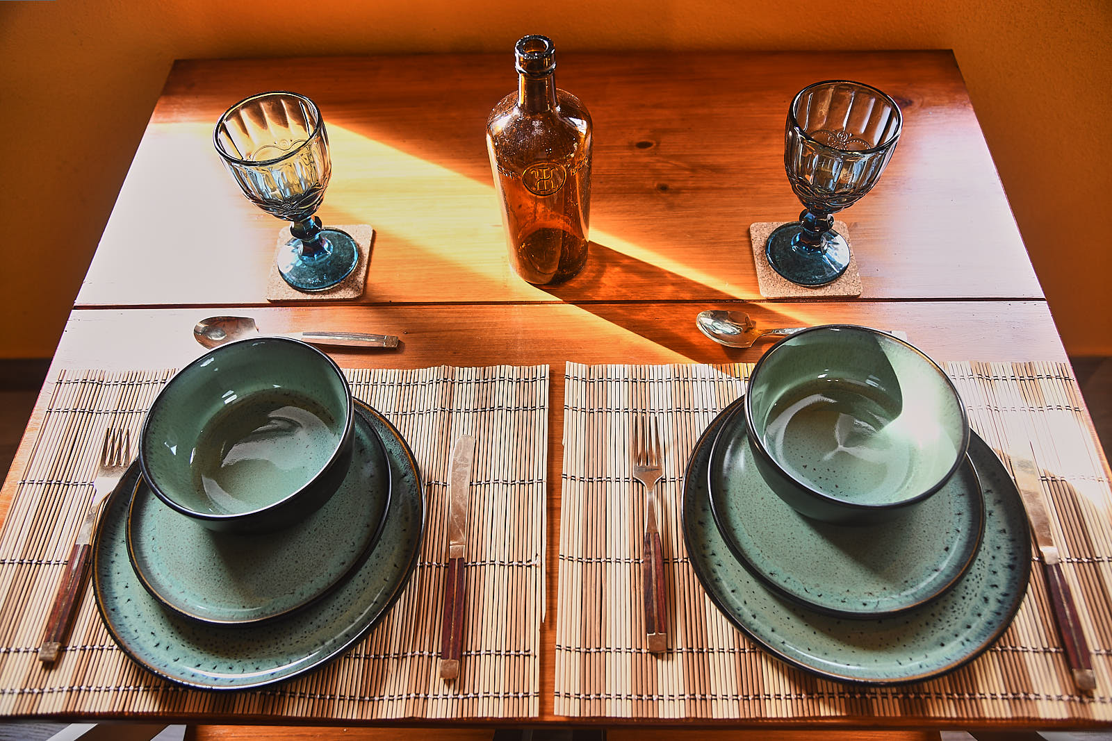 Dining table set with green ceramic bowls, blue glasses and amber bottle